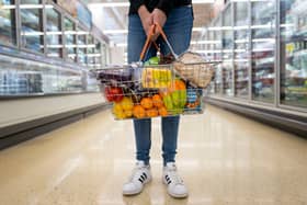 A woman holds a basket of goods in a supermarket.