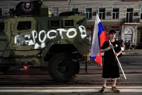 A man holds the Russian national flag in front of a Wagner group military vehicle with the sign read as "Rostov" in Rostov-on-Don late on June 24, 2023. Rebel mercenary leader Yevgeny Prigozhin who sent his fighters to topple the military leaders in Moscow will leave for Belarus and a criminal case against him will be dropped as part of a deal to avoid "bloodshed," the Kremlin said on June 24. (Photo by STRINGER / AFP) (Photo by STRINGER/AFP via Getty Images)