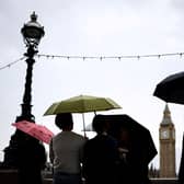 Pedestrian stand under umbrellas while looking at Elizabeth Tower, commonly called Big Ben from the Southbank by the River Thames, in central London, on July 31, 2023 on a gloomy and rainy summer day.