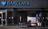 Commuters wait at a bus stop outside a branch of Barclays in London.