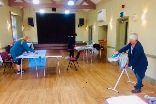 Sheila Jones then Monika Morgan at furthest at the cutting table and Adrienne Obard at the ironing board at the Ratley Village Hall