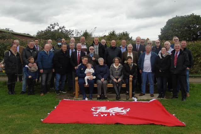 Some  of  Roy Davies’ family sitting on the new memorial bench, joined by members of Rugby Welsh, with the club flag in front. The bench is inscribed with the words ‘In memory of all those who loved our club - Rugby Welsh Rugby Football Club’