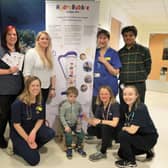 Ivan Wright pictured with the HydroBubble device with Rebecca Bott (back row, second from left) and members of the Cystic Fibrosis service team, who developed the HydroBubble device.Bottom left to right – Dr Maggie Hufton (Paediatric Cystic Fibrosis (CF) Consultant, University Hospitals Coventry and Warwickshire NHS Trust (UHCW)), Ivan Wright, Annika Shepherd (Advanced Childrens Respiratory Physiotherapist, Coventry and Warwickshire Partnership NHS Trust), Grainne O’Neill (Paediatric Physiotherapist, UHCW). Top left to right – Jane White (CF Nurse, Community Children's Nursing (CNN) Team South Warwickshire University NHS Foundation Trust), Rebecca Bott (Mum of Ivan), Yasmin Hussaini (CF Nurse, CCN Team South Warwickshire University NHS Foundation Trust) and Dr Rajesh Srikantaiah (Paediatric CF Consultant, UHCW). Photo supplied