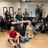 In front of the keyboard are Kevin Bright (teacher/parent/Stanley), Kirsty Bright (KC/teacher) and assistant director Emma Bright; behind the keyboard are Mabel Watson (Katie Travis, team Stick It To The Man), musical director Jon Watson and Matt Watson (Dewey Finn, team Stick It To The Man); on the left behind the drums in checked shirt is Rafferty Jones (Freddy Hamilton, team Stick It To The Man) with Leanne Jones (parent/teacher) in front of him; on the right behind drums is Riley Withall (Freddy Hamilton, team Mount Rock) and Gwen Withall (parent/ JJ/ school staff) in front of him; next to her are Sophie Jones (Mrs Sheinkopff) and Alfie Jones (Billy Sandford, Team Mount Rock); and on the right are Dexter Robinson (Zack Mooneyham, team Stick It To The Man) and director Kenny Robinson. Not in the photo are Poppy Goodwin (Lauren Turner, team Stick it to the Man) and Dave Goodwin (parent / teacher).