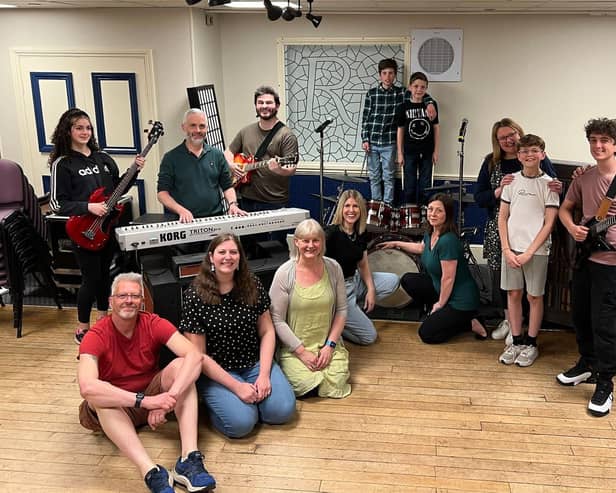 In front of the keyboard are Kevin Bright (teacher/parent/Stanley), Kirsty Bright (KC/teacher) and assistant director Emma Bright; behind the keyboard are Mabel Watson (Katie Travis, team Stick It To The Man), musical director Jon Watson and Matt Watson (Dewey Finn, team Stick It To The Man); on the left behind the drums in checked shirt is Rafferty Jones (Freddy Hamilton, team Stick It To The Man) with Leanne Jones (parent/teacher) in front of him; on the right behind drums is Riley Withall (Freddy Hamilton, team Mount Rock) and Gwen Withall (parent/ JJ/ school staff) in front of him; next to her are Sophie Jones (Mrs Sheinkopff) and Alfie Jones (Billy Sandford, Team Mount Rock); and on the right are Dexter Robinson (Zack Mooneyham, team Stick It To The Man) and director Kenny Robinson. Not in the photo are Poppy Goodwin (Lauren Turner, team Stick it to the Man) and Dave Goodwin (parent / teacher).