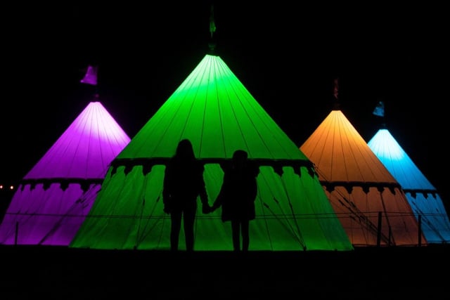 A tent encampment is illuminated with multicoloured lights along the Christmas trail