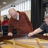 Steve Droy, professional concert piano tuner and founder of the Piano Technology School, works on the baby grand piano at the Benn Hall with students Eoin McCarthy (left) and Henry Melbourne (right)