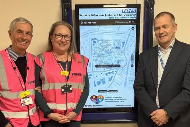 Nigel Corcoran (pictured right) and Trust volunteers, Jim and Cheri (L-R), with the Living Map screen at Warwick Hospital. Photo supplied.