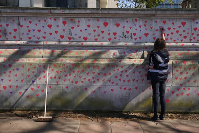 A woman painting red hearts on the COVID-19 Memorial Wall opposite the Houses of Parliament at Embankment, central London, in memory of the more than 145,000 people who have died in the UK from coronavirus. Picture date: Monday March 29, 2021.