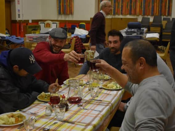 Shelter users toast with glasses of squash as they enjoy a home-cooked vegetable stew.