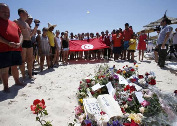People, some displaying a Tunisian flag, stand in silence next to flowers during a gathering at the scene of the attack in Sousse, Tunisia, Sunday, June 28, 2015. The Friday attack on tourists at a beach is expected to be a huge blow to Tunisia's tourism sector, which made up nearly 15 percent of the country's gross domestic product in 2014. (AP Photo/Abdeljalil Bounhar) EMN-150629-180457001